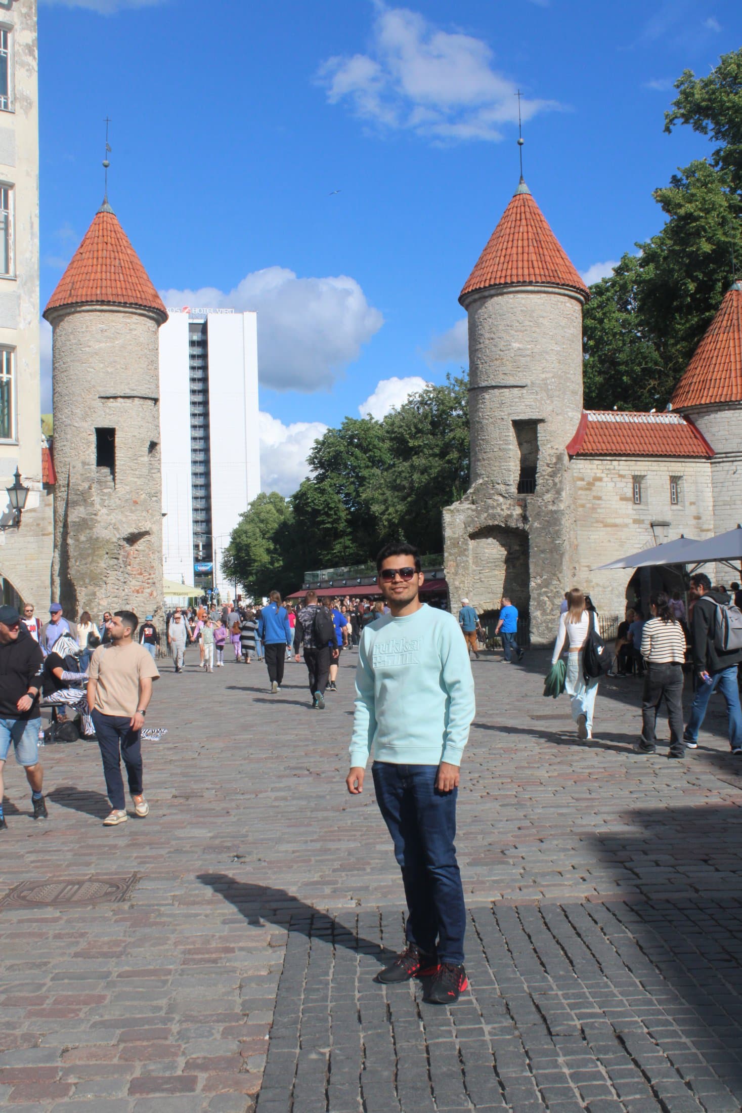 Shivam standing between the twin medieval towers of the Viru Gate in Tallinn's Old Town under a blue sky.